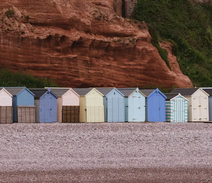 Beach huts on the pebble beach below the red Triassic cliffs at Budleigh Salterton, where coastal exposure shapes window specification and cost