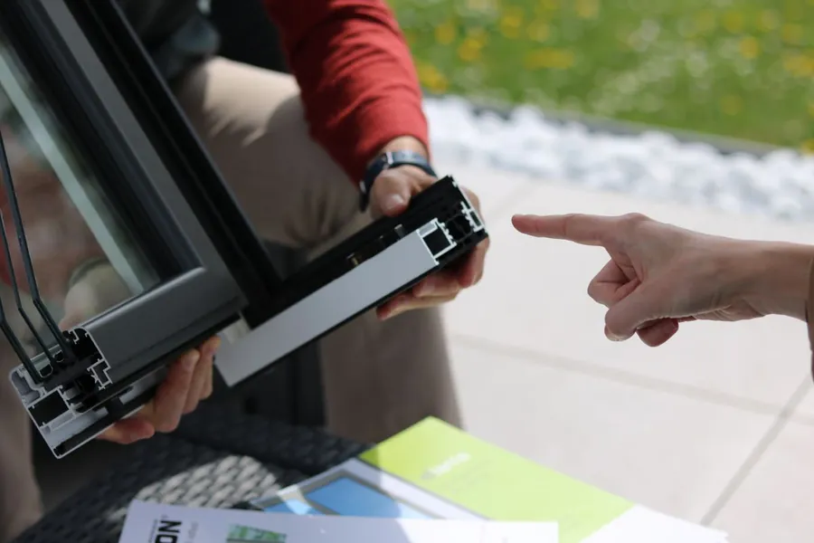Installer showing a homeowner a cut section of an aluminium window profile when specifying coastal-grade windows for Exmouth