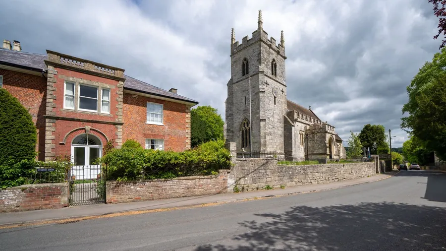 Stone parish church beside a period brick house with sash windows in an English conservation area, like the streets around Crediton's Holy Cross church