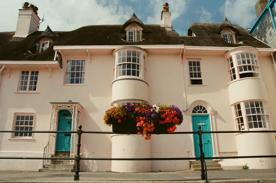 Pale painted Regency-era seaside house with curved bow sash windows, dormers and a teal front door, similar to the period frontages around Dawlish