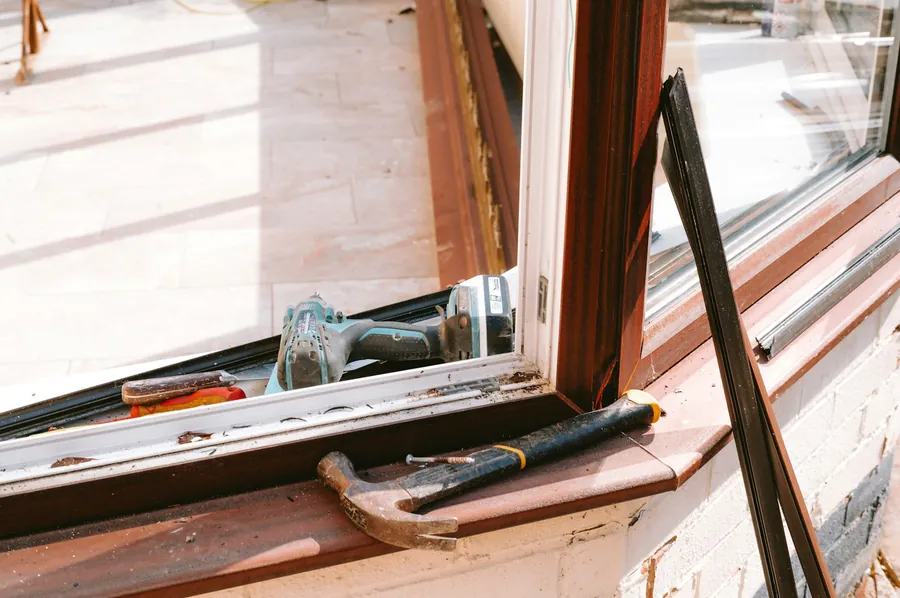 Open uPVC casement window with a drill and hammer resting on the sill during a hardware repair