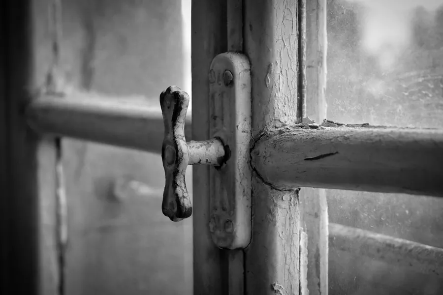 Close-up of a worn window handle and latch on an old painted frame