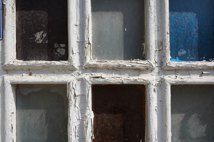 Old painted timber window frame with peeling paint from years of salt air exposure on a coastal property near Budleigh Salterton