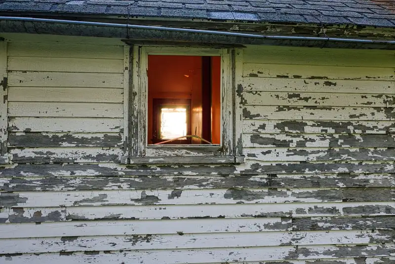 Old weathered window frame with peeling paint on a brick building - window frame deterioration and rot in Exeter properties