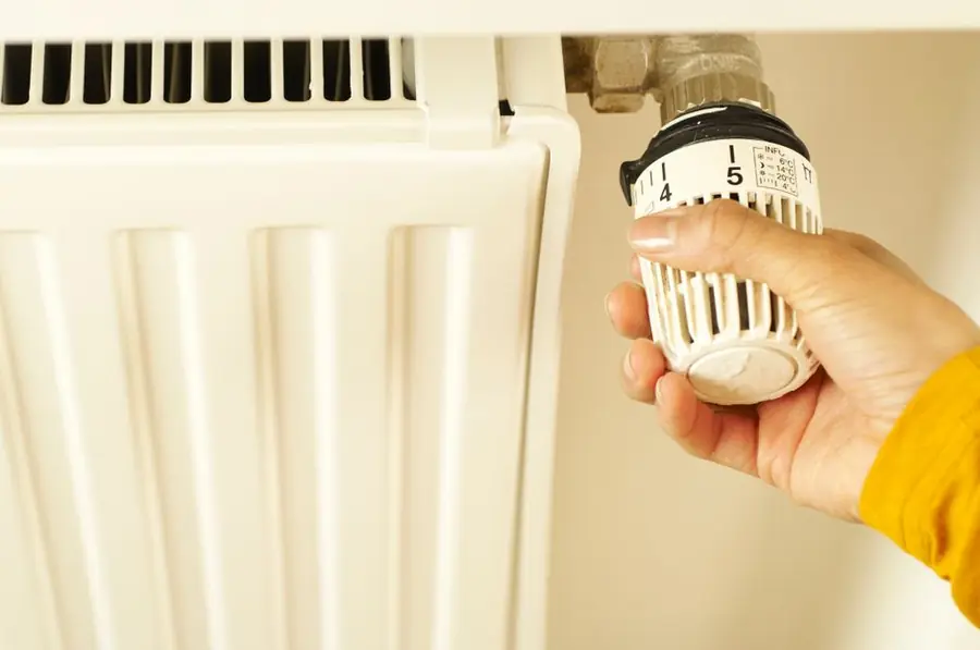 A hand adjusting a radiator thermostat - failed windows push heating bills up every winter they're left