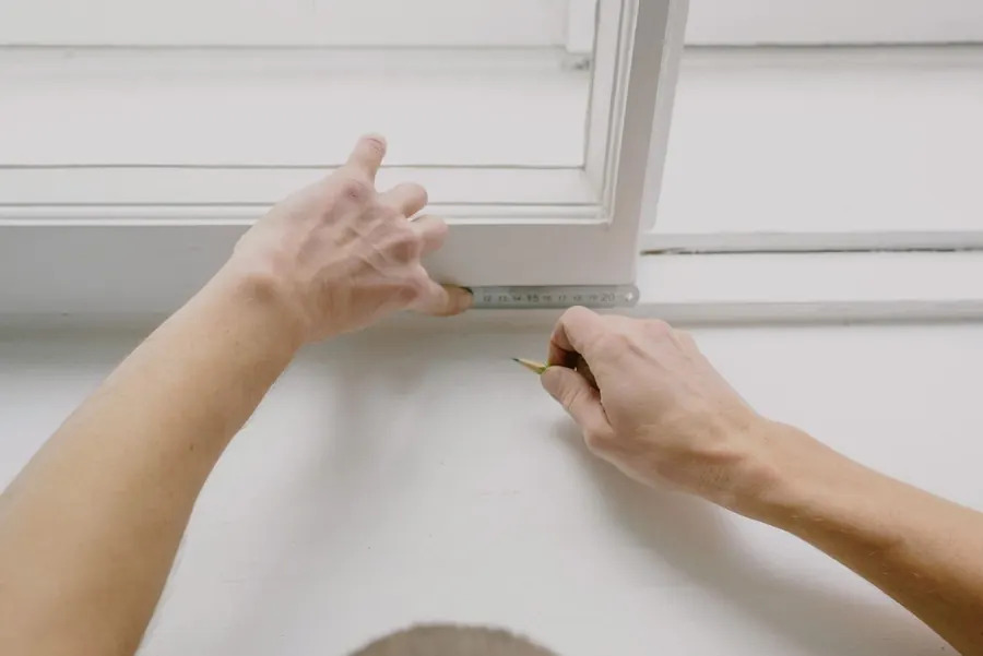 Window fitter measuring a painted window frame with a steel rule before quoting a replacement window in a Crediton home